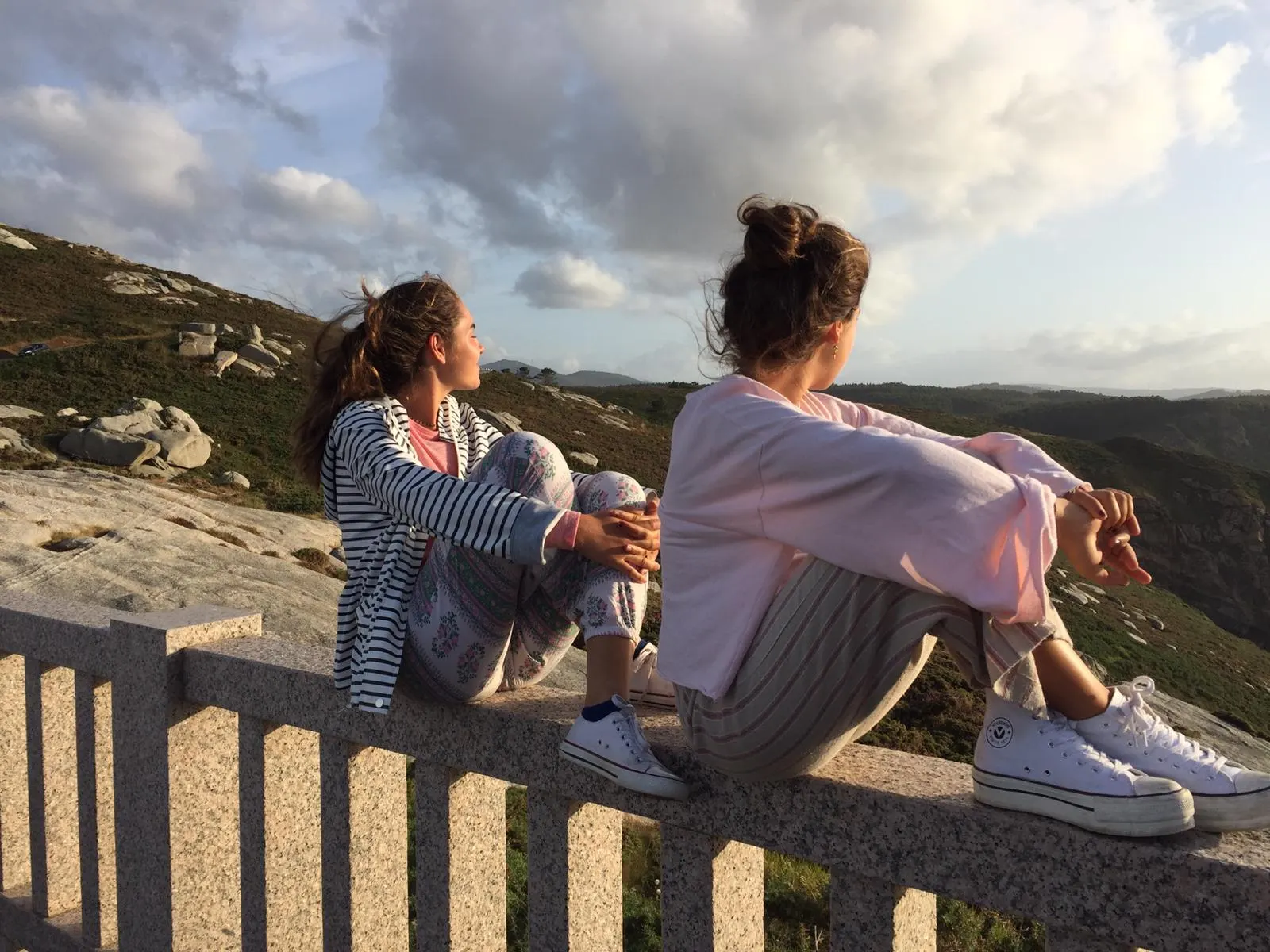 Raquel and a friend sitting on a stone wall looking over a valley