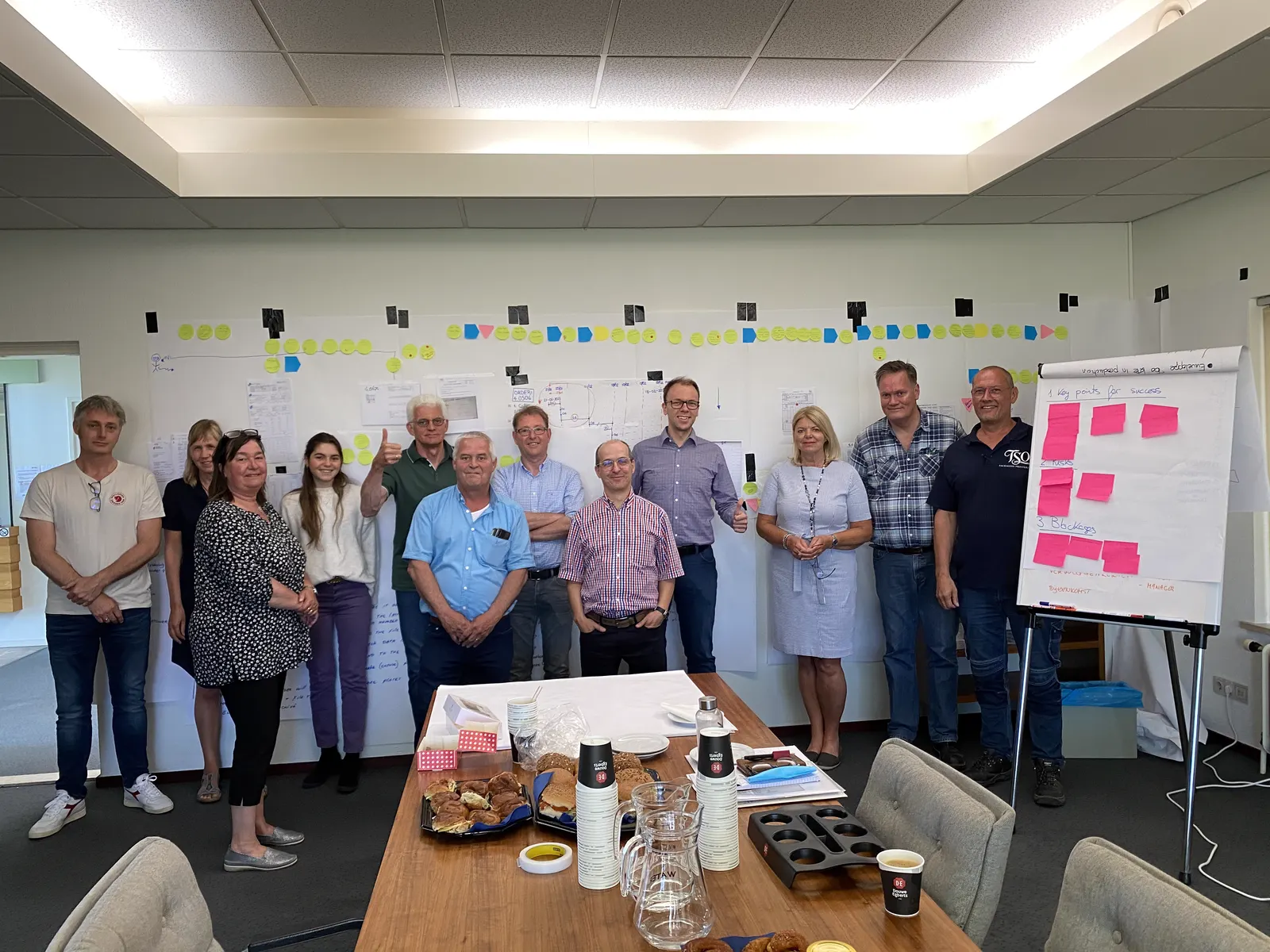 The improvement project team standing in a meeting room in front of a wall of process maps