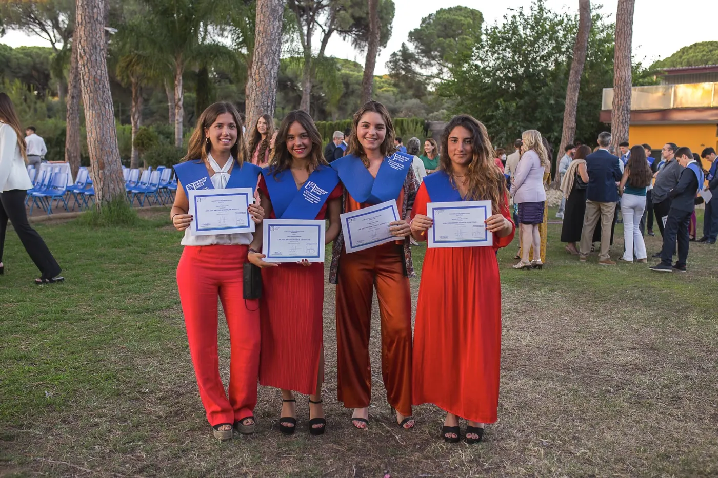 Raquel with three classmates holding their school graduation diplomas
